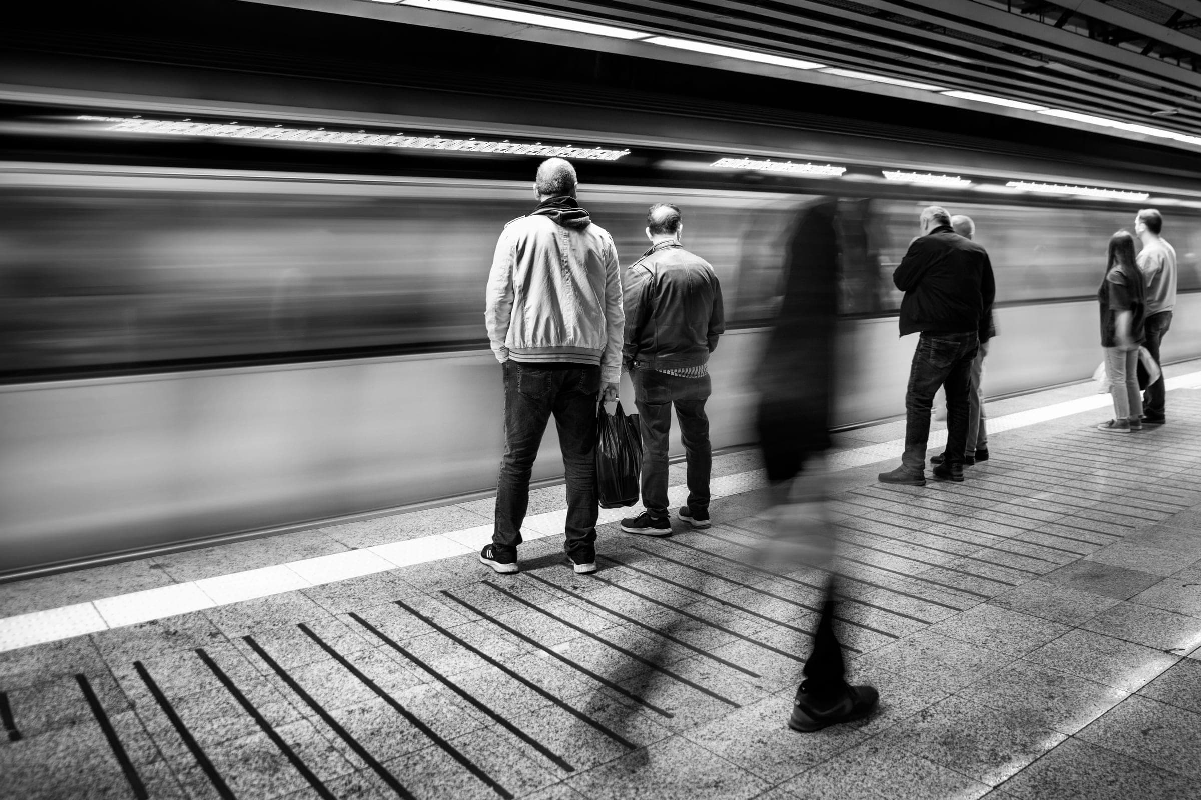 Commuters standing still on a subway platform as a train blurs past